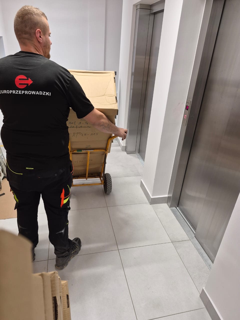 Pracownik przewożący kartony wózkiem transportowym